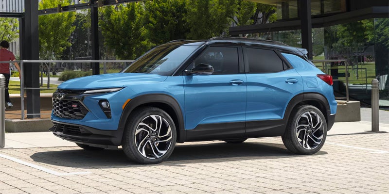 A blue Trailblazer parked on a paved walkway outside a modern glass building.